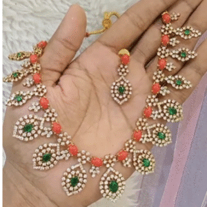 Gold-plated traditional necklace set with red beads, white stones, and green Kundan drop design, displayed on a hand along with a matching earring