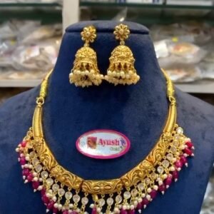 Bridal Kundan gold necklace set with red beads and matching jhumka earrings displayed on blue velvet stand